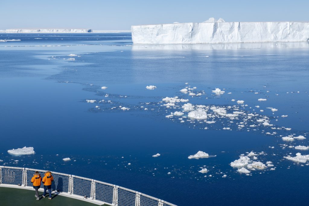 The bow of a ship sailing towards large tabular iceberg. 