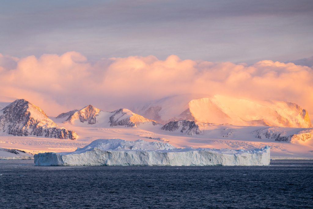Tabular iceberg and snow covered peaks at sunrise. 