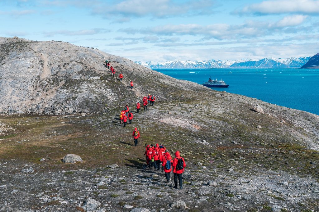 Passengers hiking shoreline with ship in the background. 