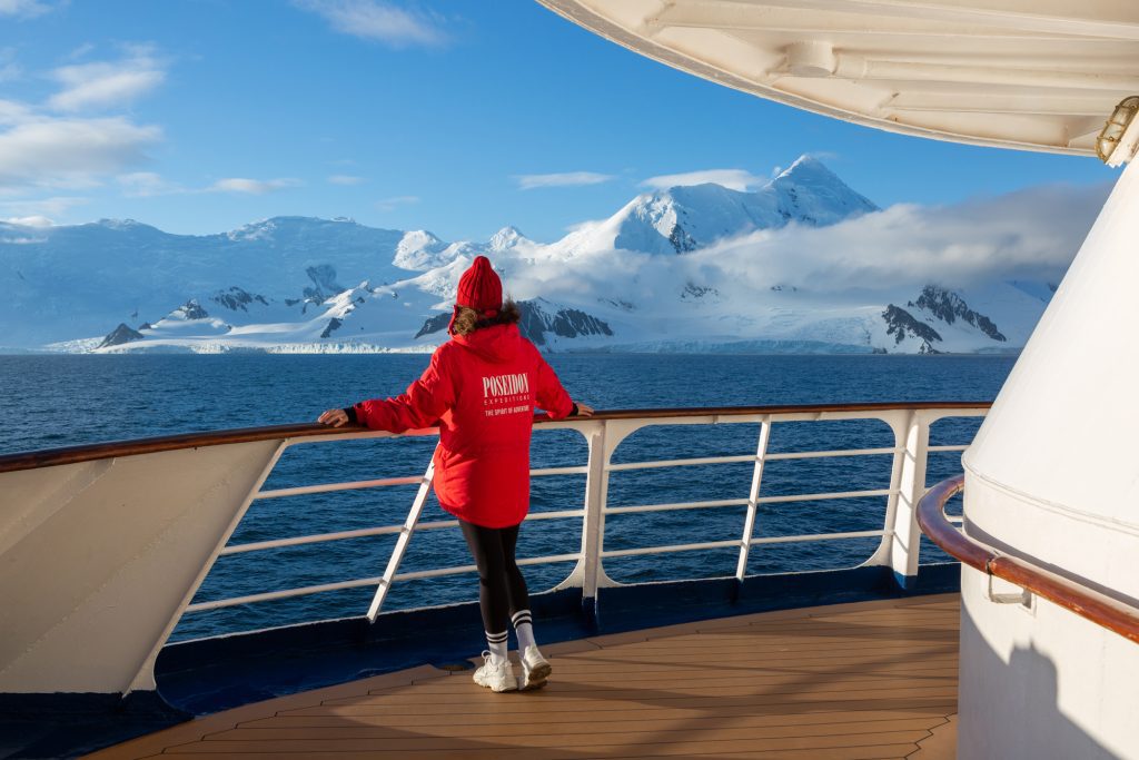 Guest standing on deck of ship looking at snow covered mountains. 