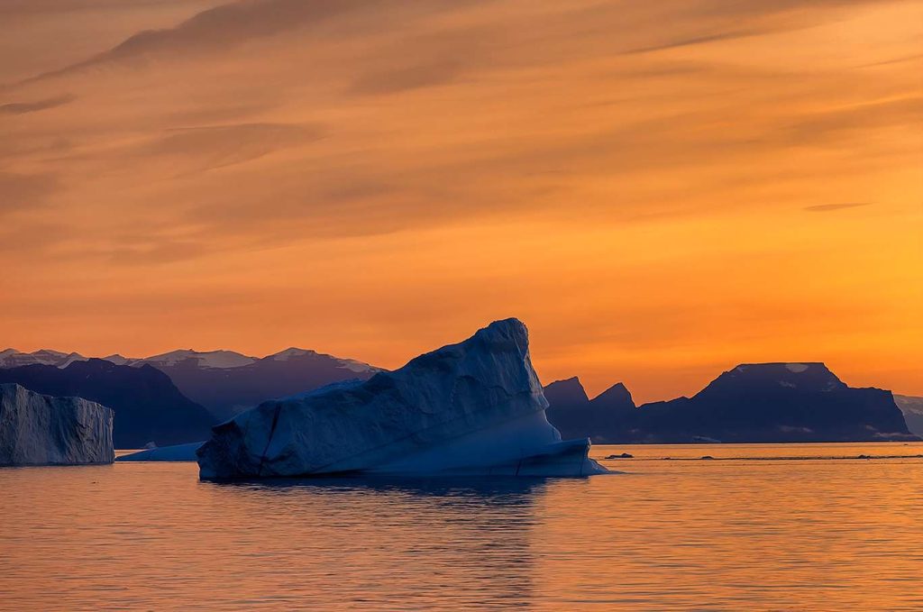 An iceberg with an orange sky at sunset.