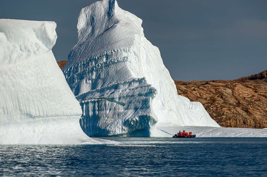Zodiac cruising past massive iceberg in East Greenland.