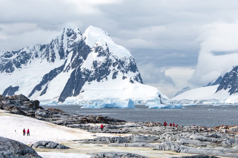 Passengers on shore with penguins and mountain in background on Antarctica Classic itinerary