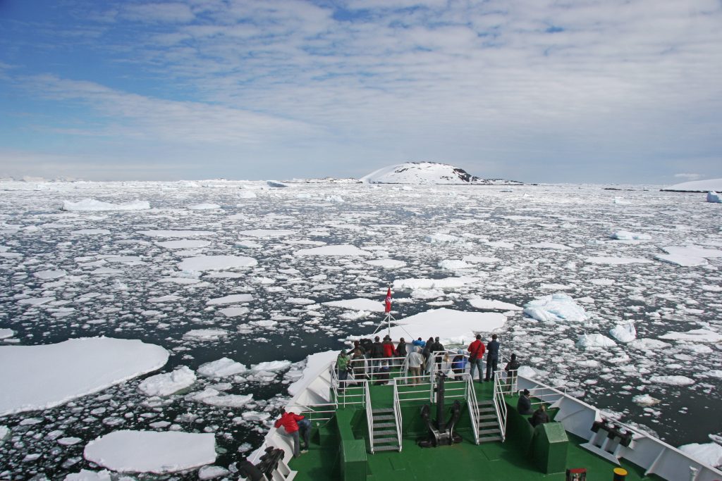 Guests standing on bow of ship looking at icy waters. 