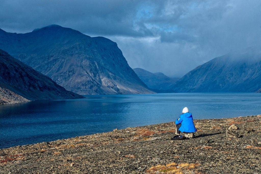 Guest sitting on tundra in dramatic fjord.