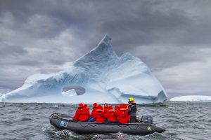 Guests on a zodiac in front of large iceberg. 