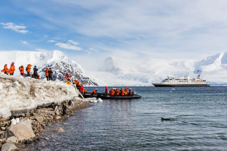 Guests disembarking the zodiacs onto shore in Antarctica with the National Geographic Orion in background