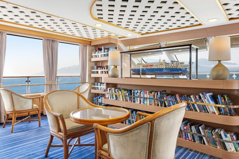 National Geographic Orion observation lounge & library with table, books and large windows.