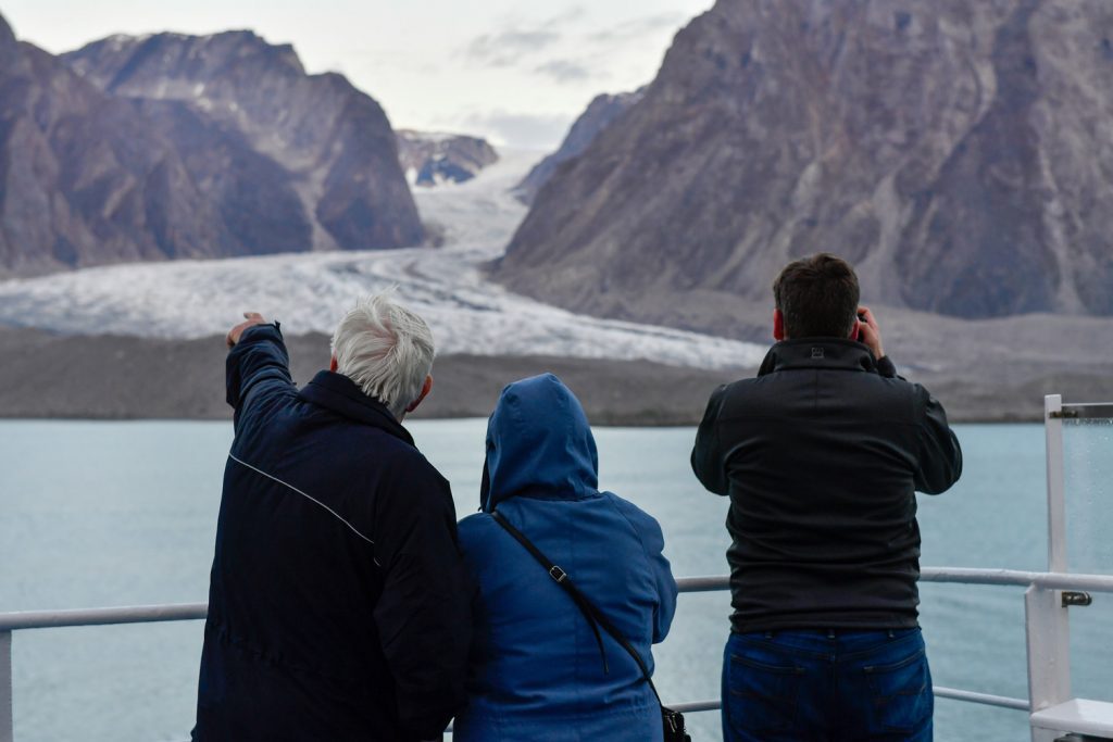 Guests standing on deck of ship gazing at flowing glacier. 