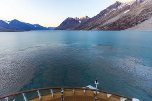 The bow of a ship sailing into a scenic fjord. 