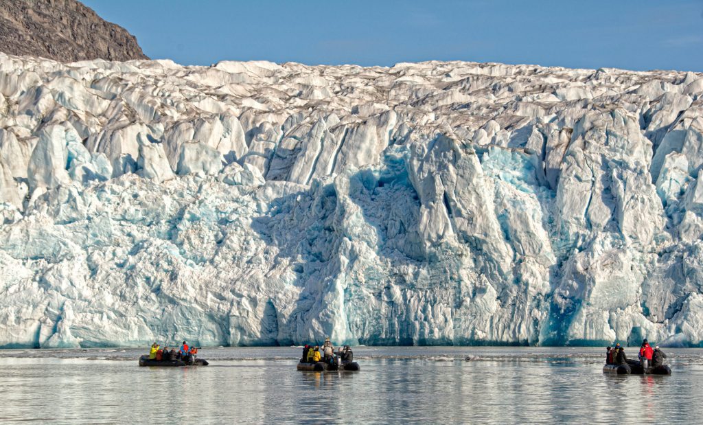Three zodiacs on the water in front of large glacier face. 