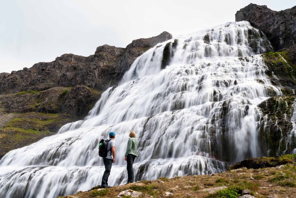 Two guests standing in front of large waterfall. 