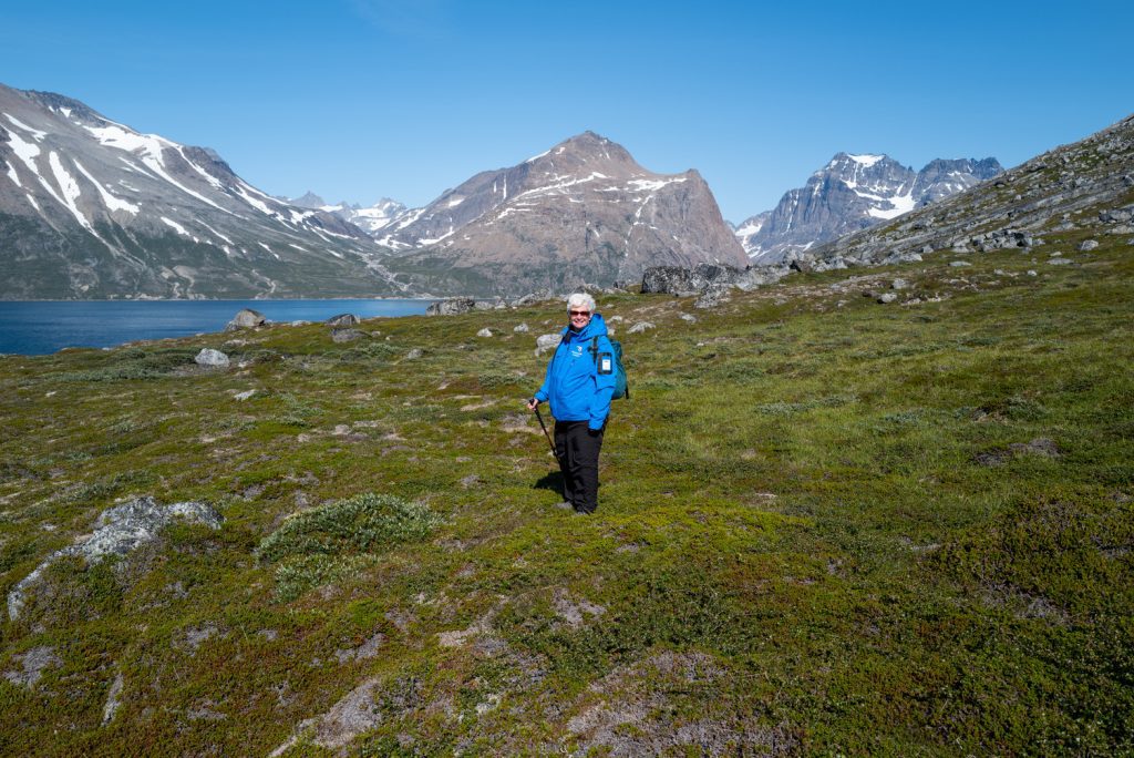 Guest standing on tundra in front of scenic mountains in Greenland. 