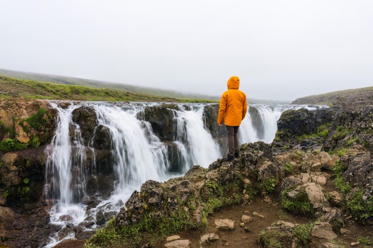 Male tourist standing and looking at Kolugljufur Canyon rapids f