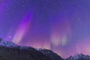 Pink northern lights shining above snow covered mountains