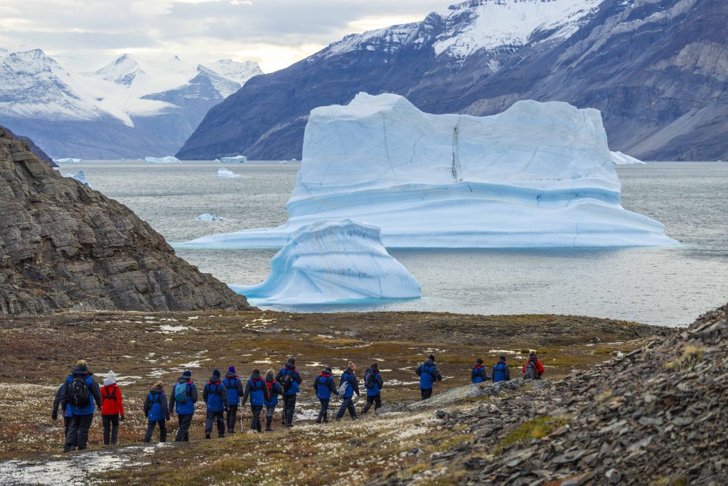 A line of hikers with huge iceberg in background.