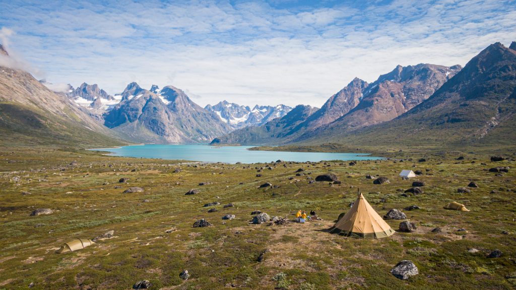 Tents in tundra next to lake and mountains in Greenland. 