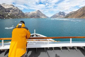 Passenger on deck of ship looking at scenic Greenland landscape. 