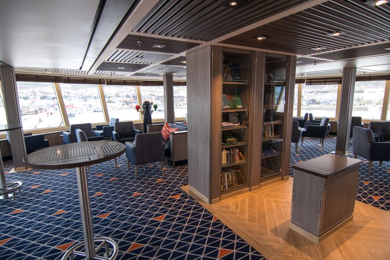 Observation lounge with large windows, chairs and bookcase on Silver Cloud.