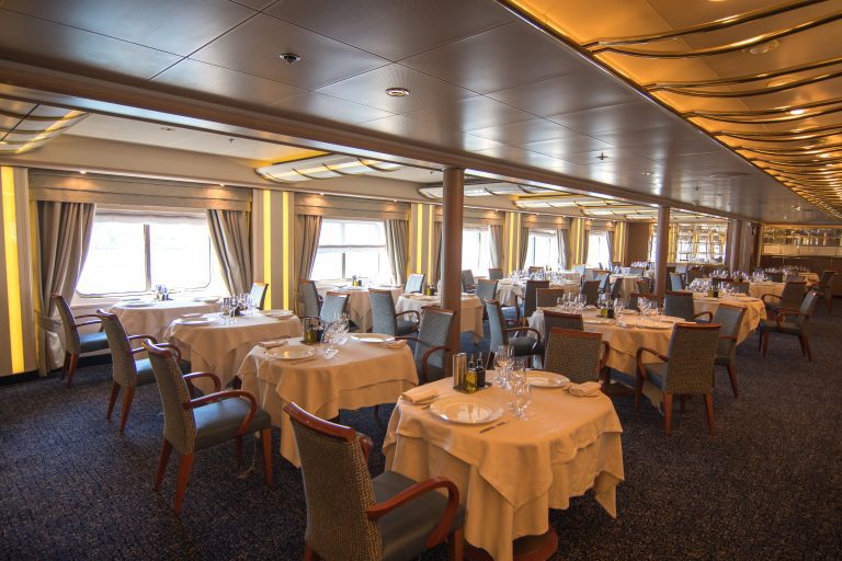 Main restaurant on Silver Cloud with multiple tables, white table clothes and large windows.