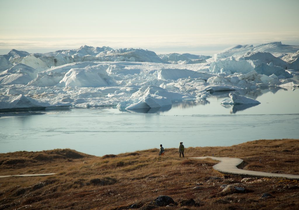 Guest hiking on trail next to massive icebergs in West Greenland.