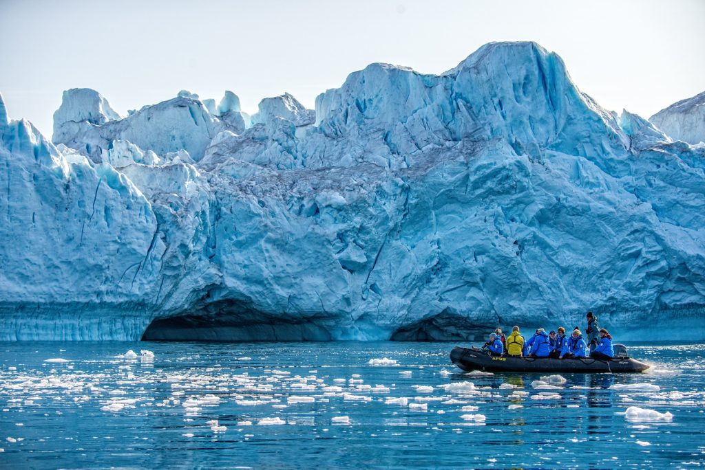Zodiac cruising near large iceberg in Greenland. 