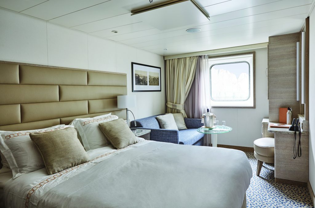 Bedroom with queen bed and large window in Ocean Stateroom on Exploris One. 