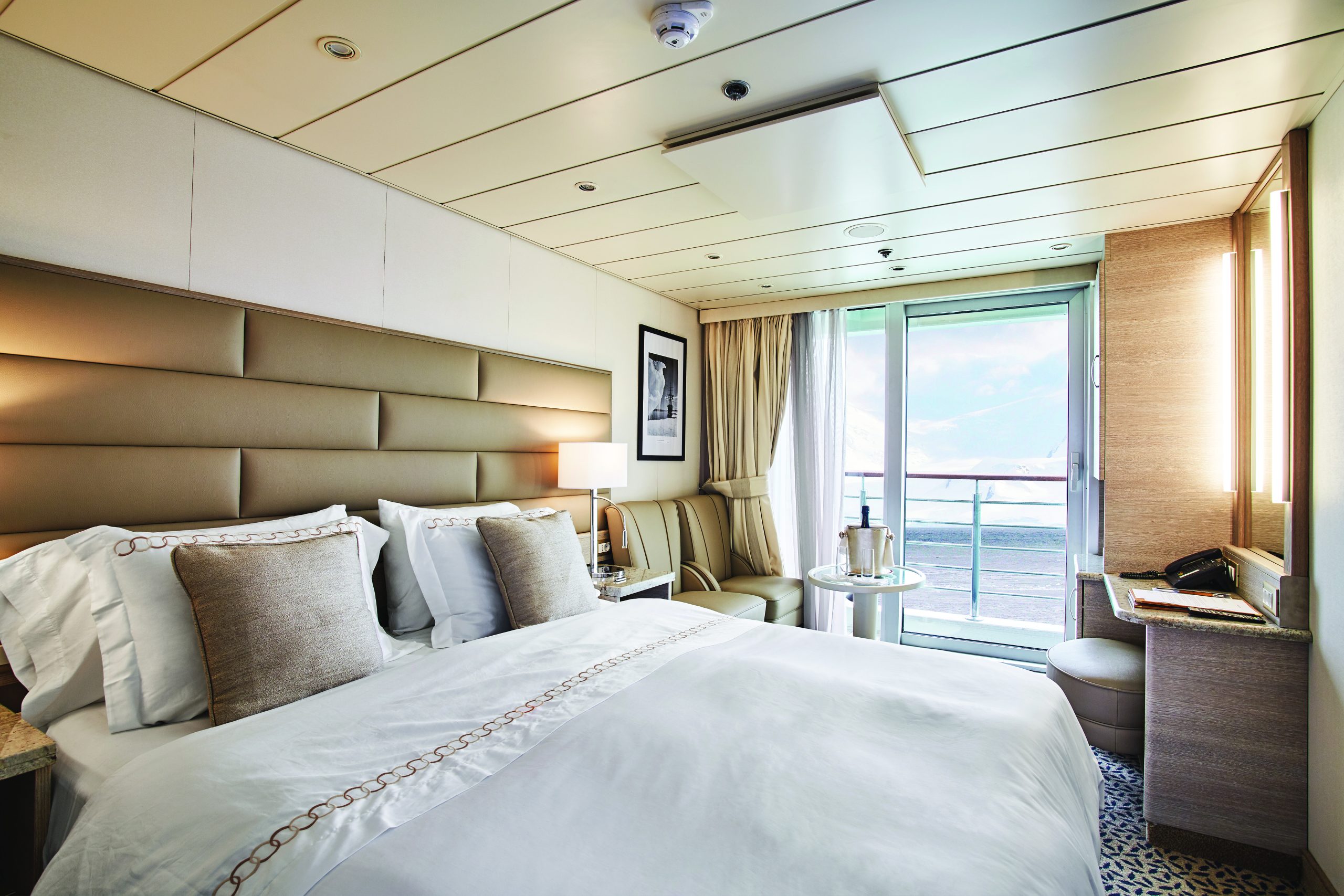 Balcony Stateroom onboard Exploris One showing queen bed, sitting area and private balcony.