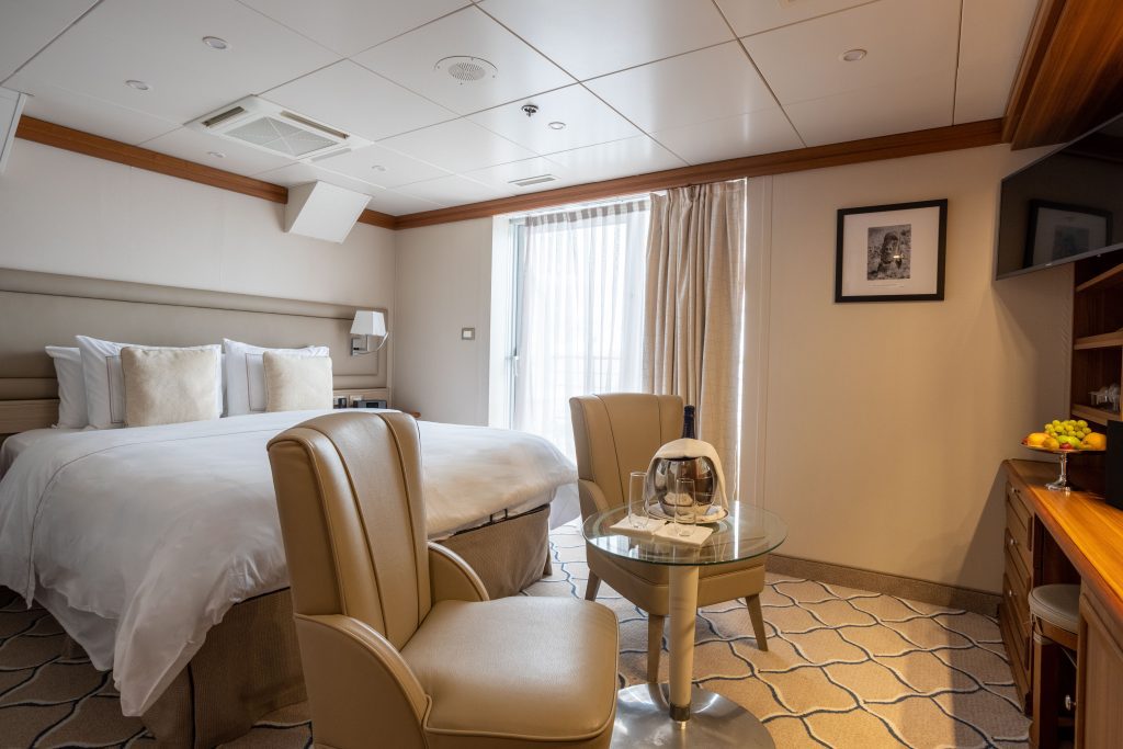 Queen bed, 2 chairs and small table in Navigator Suite on Exploris One.