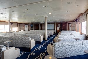 The Lecture Lounge on Discoverer with rows of bench seating, large TV and windows.