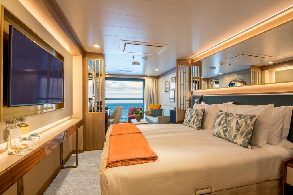Infinity Suite on World Voyager with bed, small couch and floor to ceiling window. 