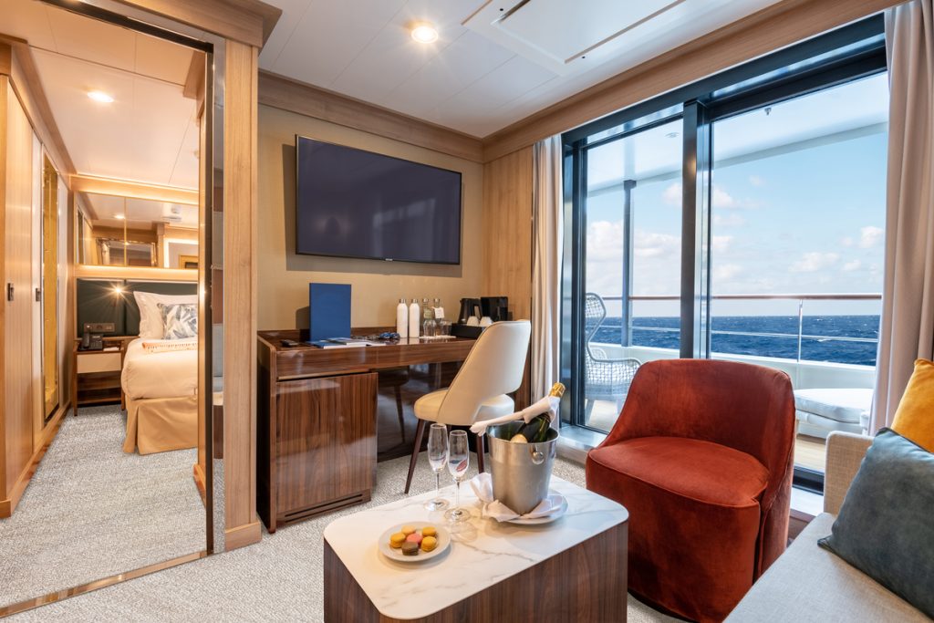 Superior Suite on World Voyager with sitting area, desk, balcony and door leading to bedroom. 