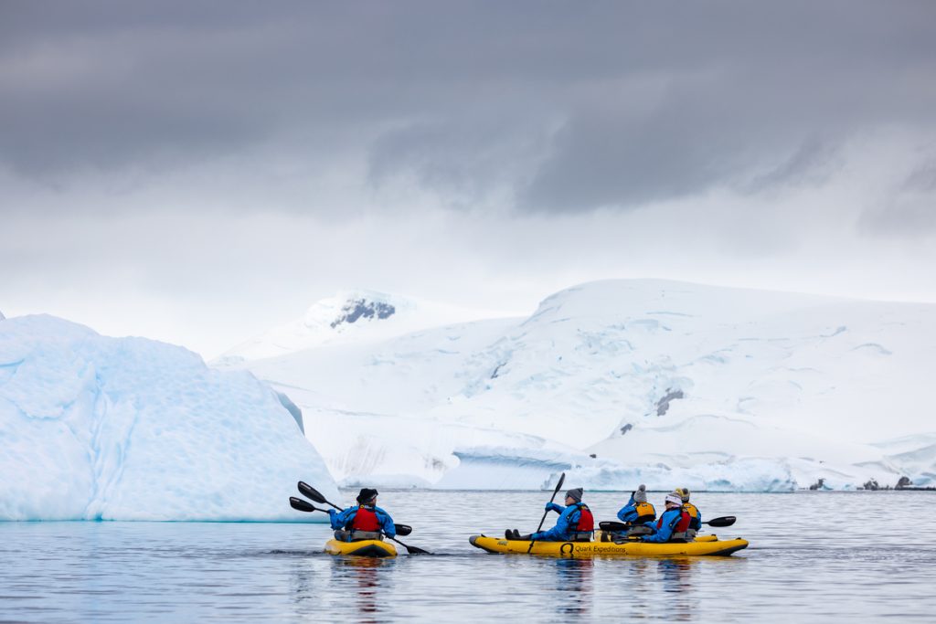 Kayakers paddling near iceberg in Antarctica. 