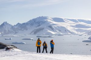 Three passengers standing on snow in Antarctica. 