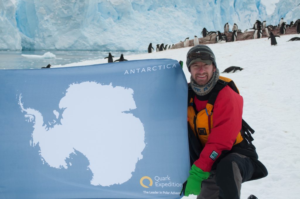 Guest holding Antarctica flag with penguins in background.
