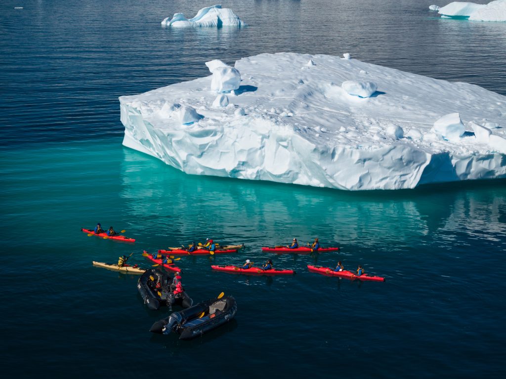 Kayaks on the water next to an iceberg. 
