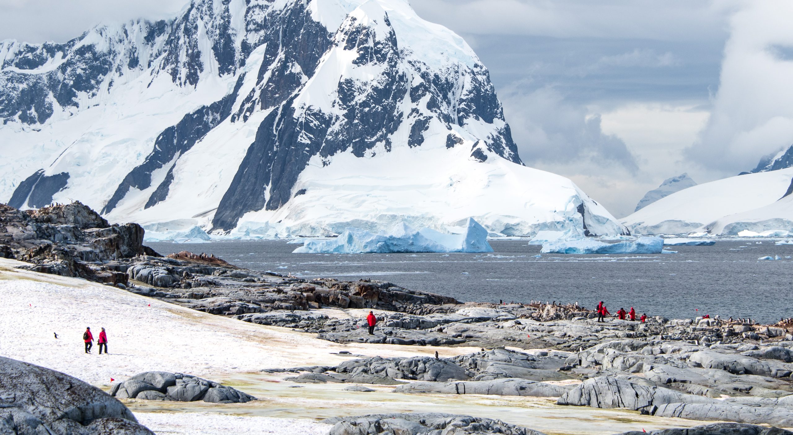 Antarctic landscape with rugged mountain, icebergs and guests on shore.