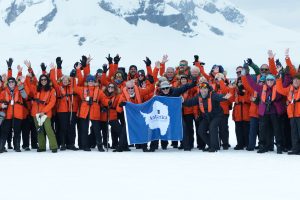 Group of passengers standing on ice holding Antarctica flag.