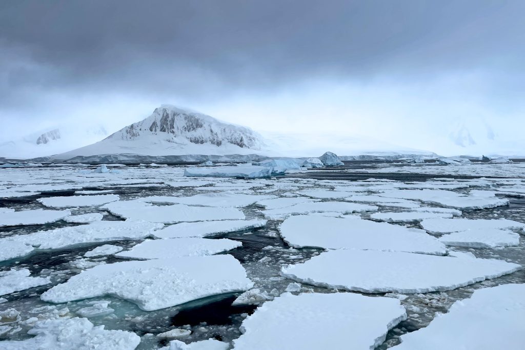White ice floes on the water with mountain in background.