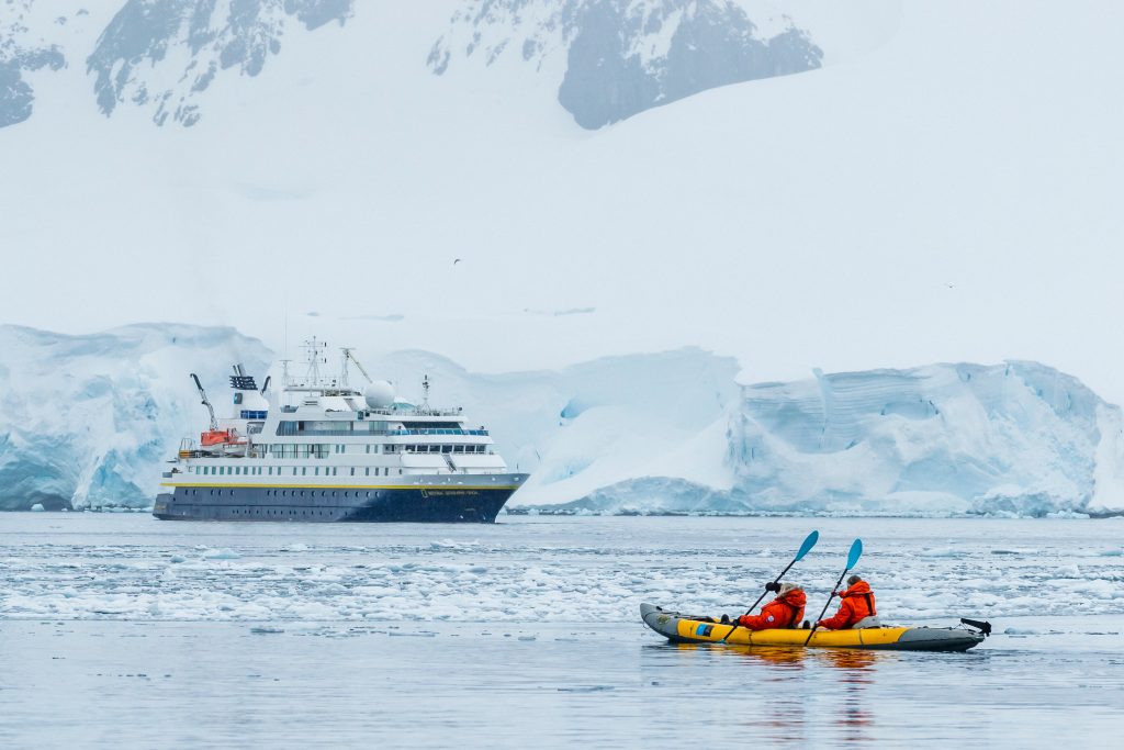 Kayakers and ship on the water with glacier face in background.