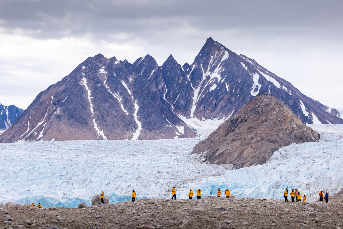 Guests hiking in front of glacier face and rugged mountains.