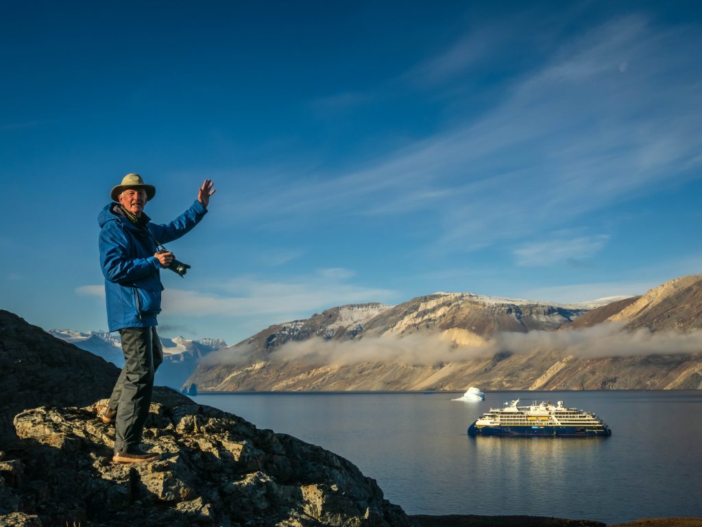 A guest waving to camera while hiking in East Greenland.