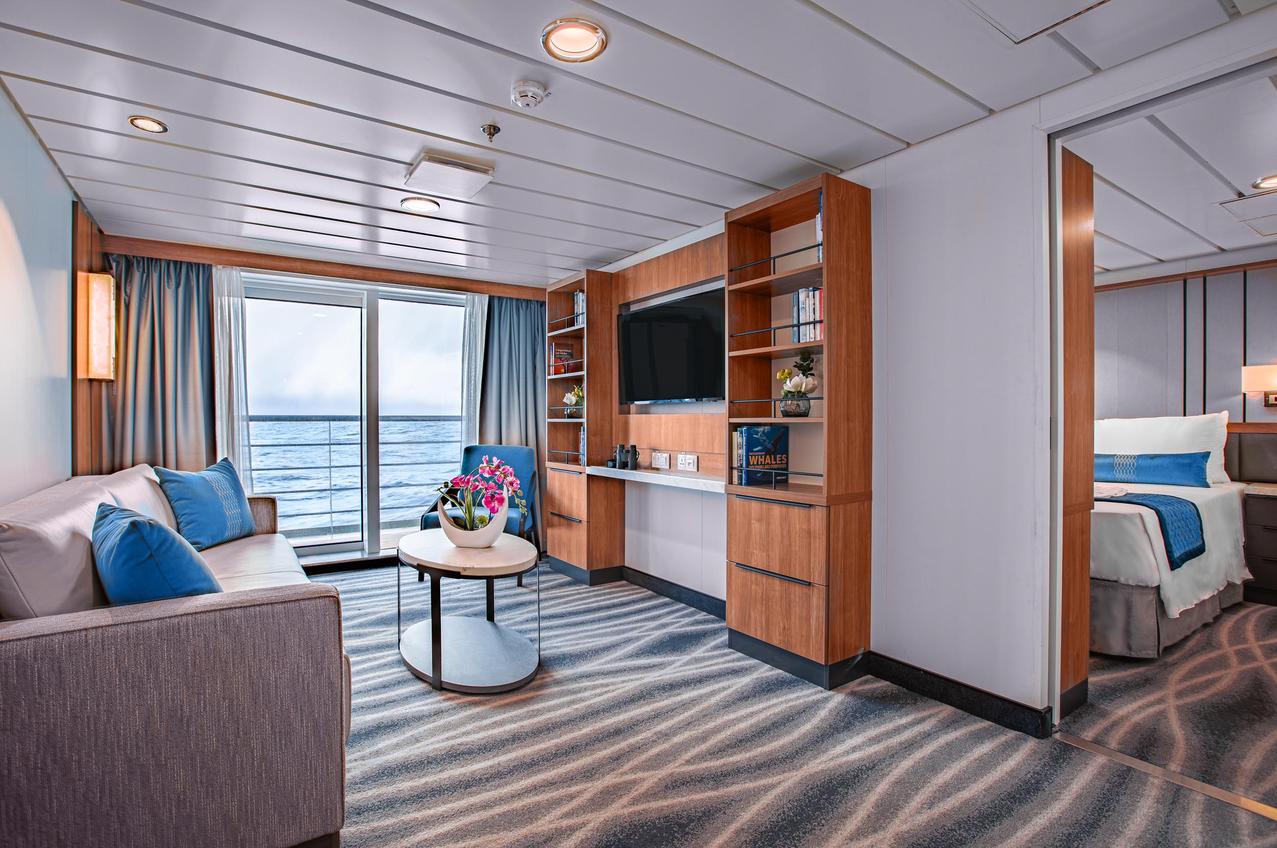 Premium Suite on Ocean Victory showing sitting area, sliding floor to ceiling glass door with ocean view and a bedroom.
