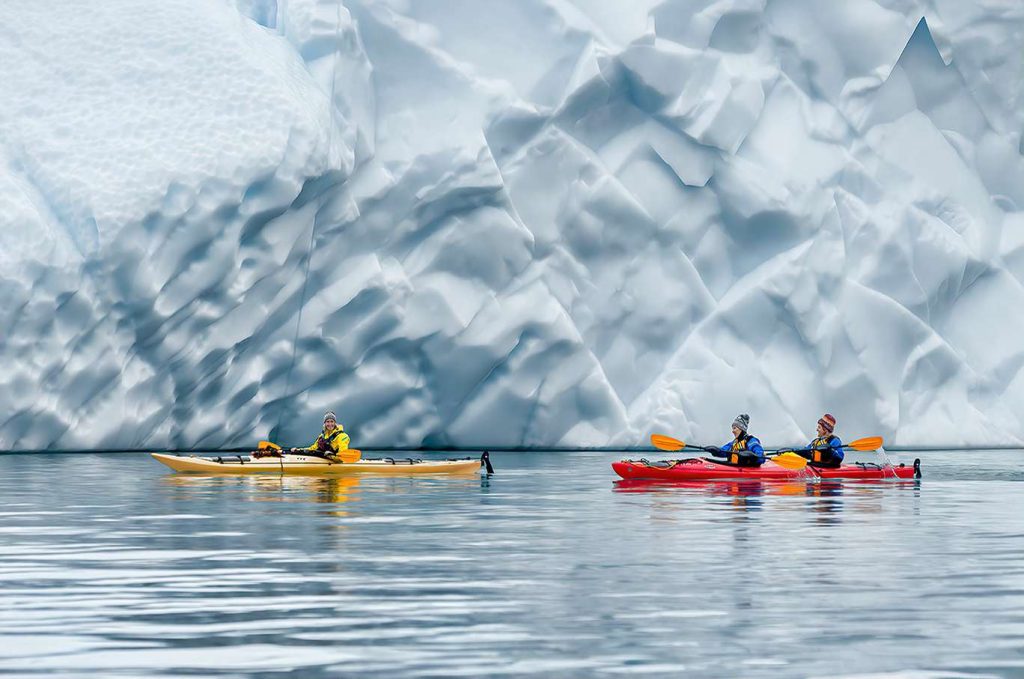Kayakers on the water in front of massive ice wall.