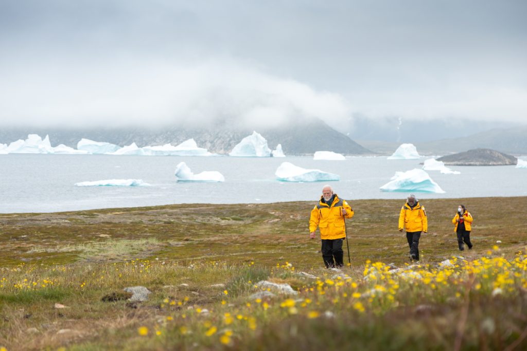 Guests hiking on shore with icebergs in background.