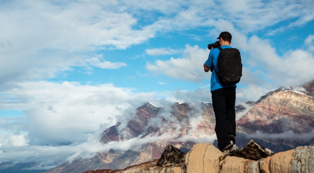 Guest standing on rock photographing scenic fjord in East Greenland. 