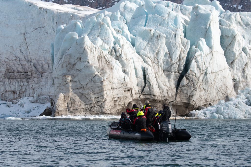 A zodiac full of guests on the water next to large glacier face. 