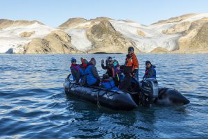 Guests waving to camera in a zodiac on the water.