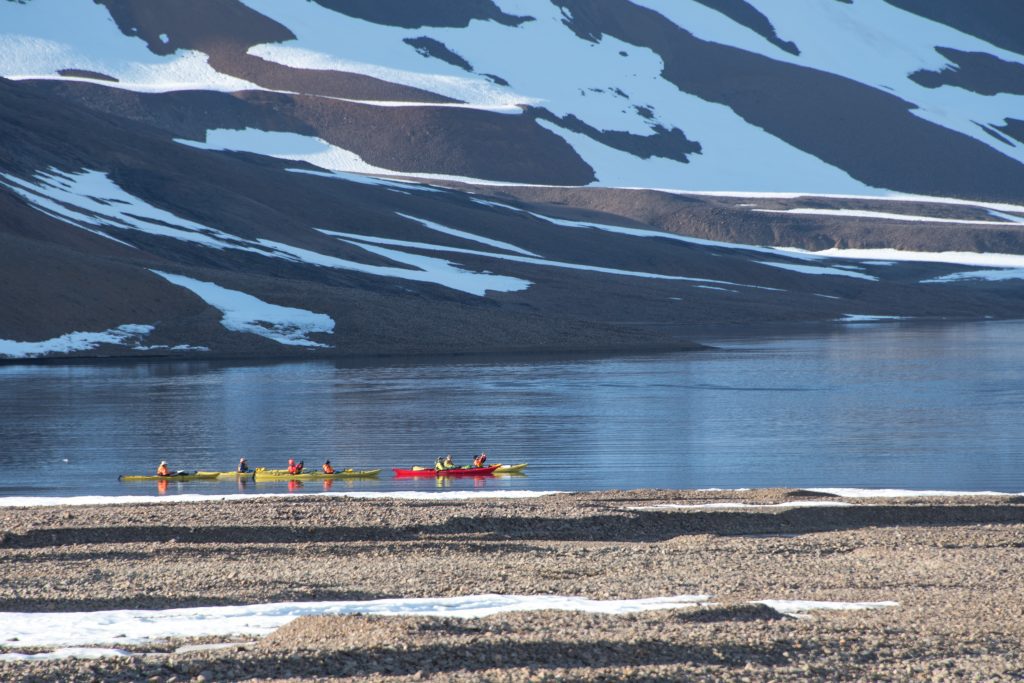 Kayakers paddling along rocky shoreline in East Greenland.