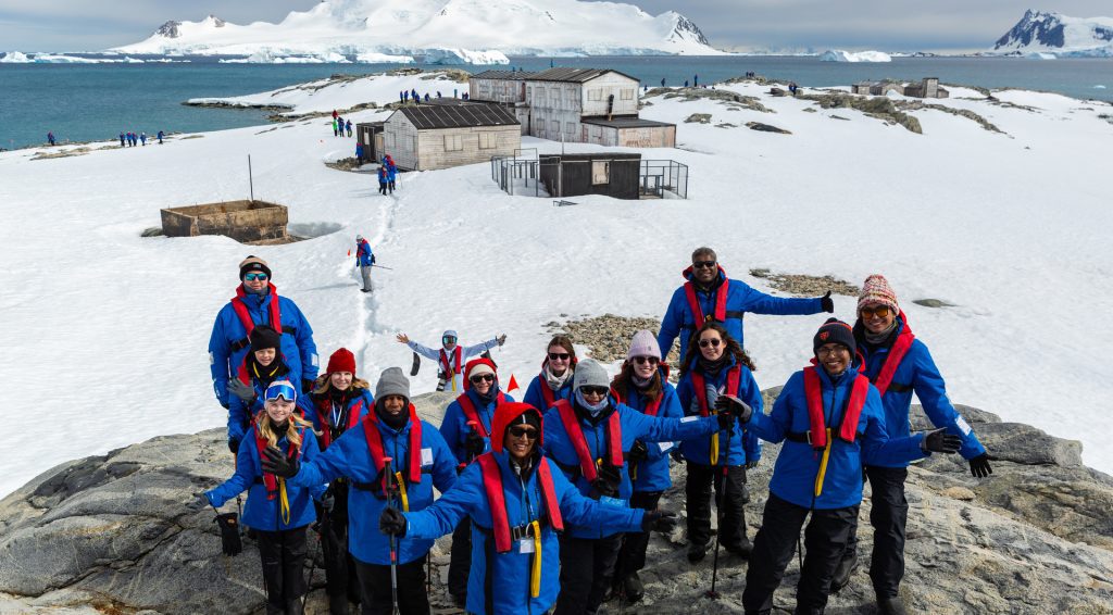 Guest standing on shore in front of old wooden buildings in Antarctica. 